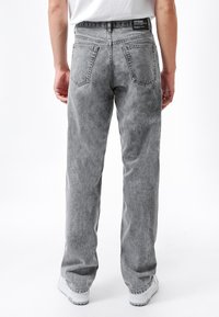 Pantalones vaqueros de mezclilla gris con un corte cómodo, que presentan una textura desgastada, cinco bolsillos y una etiqueta negra en la cintura. Sin patrones visibles.