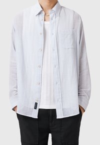 Vaaleansininen, raidallinen nappipaita pitkillä hihoilla, jossa on yksi rintatasku ja pehmeä rakenne, valkoisen aluspuseron päällä.