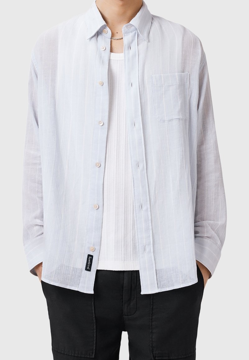 Vaaleansininen, raidallinen nappipaita pitkillä hihoilla, jossa on yksi rintatasku ja pehmeä rakenne, valkoisen aluspuseron päällä.