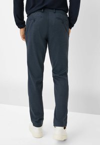 Pantaloni grigi scuri dal taglio rilassato con una finitura testurizzata, cintura elastica e due tasche posteriori con bottoni. Abbinati a sneakers bianche.