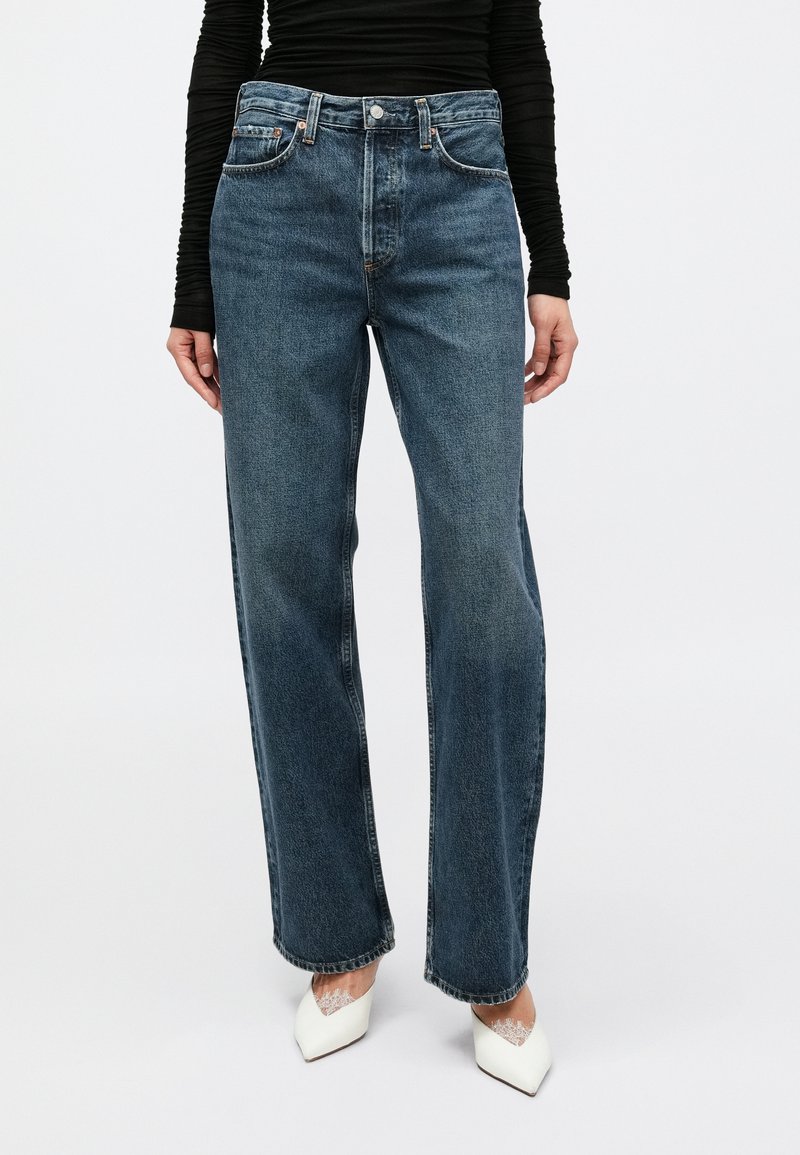 Τζιν ψηλόμεσα, φαρδιά μπατζάκια σε μεσαίο μπλε ντένιμ με ξεβαμμένο φινίρισμα, με πέντε τσέπες και αντίθετη ραφή.