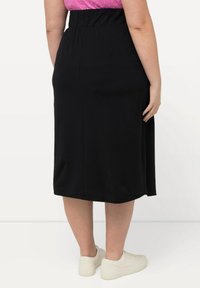 Zwarte knielange rok van zachte stof, met een elastische tailleband en een gladde, onversierde textuur. Draag het met witte sneakers.