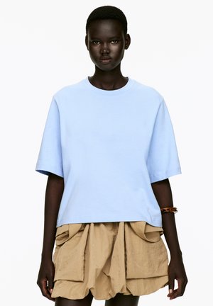 Light blue oversized cotton t-shirt with a crew neck and short sleeves, paired with a beige, textured, ruffled skirt featuring side pockets.