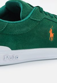 Gröna mockaskor med en vit gummisula. Anmärkningsvärt orange broderat logo på sidan och kontrasterande turkos foder.