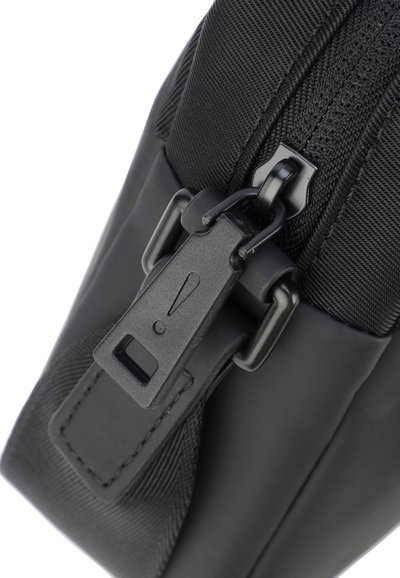Sac en tissu noir avec une finition texturée, doté d'une fermeture éclair et d'une étiquette en plastique rectangulaire avec un point d'exclamation.
