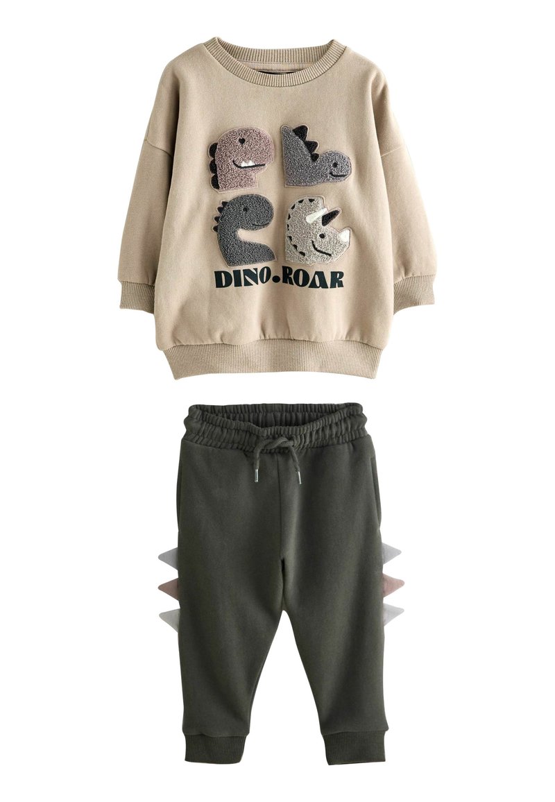 Felpa beige con applicazioni di dinosauri e testo "DINO.ROAR"; pantaloni della tuta grigi e verde chiaro con punte laterali. Tessuto morbido, design casual.