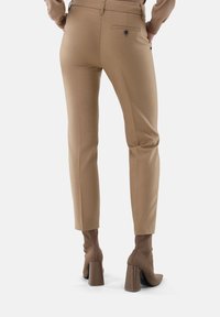 Beige maßgeschneiderte Hose mit slim fit und glatter Textur. Verfügt über eine Gesäßtasche und ein kleines schwarzes Logodetail. Kombiniert mit Stiefeletten mit Absatz.