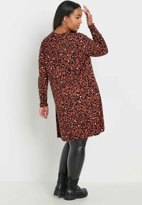 Långärmad klänning med leopardskrift i rost och svart, med rundad halsringning och lös passform, i kombination med svarta leggings i imitationläder och kraftiga stövlar.