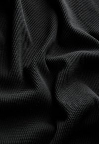 Čierna rebrovaná látka s hladkým povrchom, charakteristická výraznými vertikálnymi líniami a jemným závesom, vhodná na odevy alebo čalúnenie.