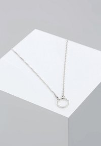 Silver necklace featuring a round pendant on a delicate chain, set against a light gray background. Minimalistic design with sleek texture.