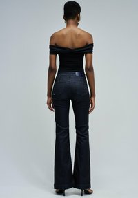 Top negro sin mangas combinado con jeans acampanados oscuros. Tejido suave con una silueta ajustada. Costuras notables y bolsillos en los jeans.