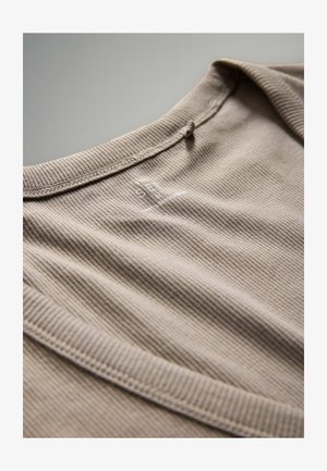 Hellbraunes, geripptes T-Shirt mit Rundhalsausschnitt, das dezentes Branding in der Nähe des Kragens aufweist. Der Stoff wirkt weich und strukturiert.