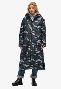 Kurtka w kamuflażu w ciemnoniebieskich, szarych i czarnych odcieniach z zamkiem z przodu, bocznymi kieszeniami i kapturem. Posiada metkę z logo.