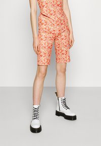 Shorts à motif floral dans des teintes d'orange et de blanc, associés à des bottes de combat blanches à lacets avec une semelle noire et un détail de fermeture éclair.
