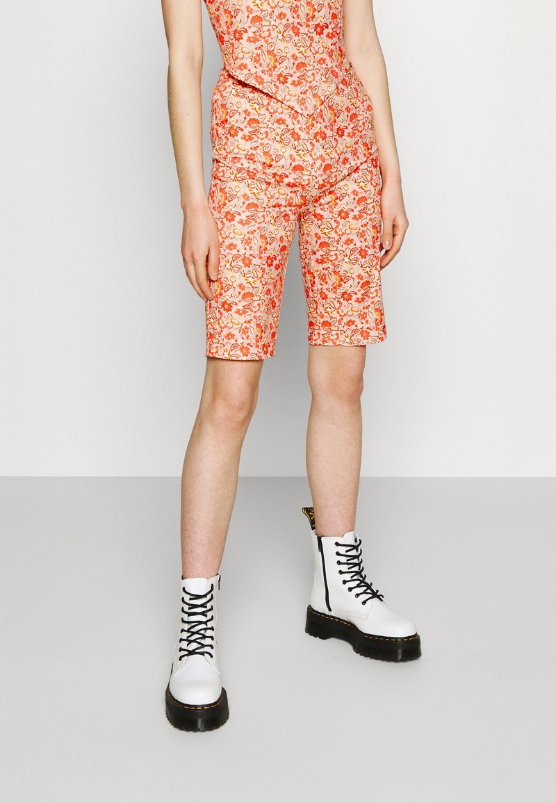 Shorts à motif floral dans des teintes d'orange et de blanc, associés à des bottes de combat blanches à lacets avec une semelle noire et un détail de fermeture éclair.