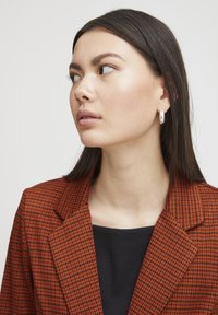 Gecheckte blazer in oranje en zwarte stof, met een notch lapel en een getailleerde pasvorm. Draag het over een zwarte top, met zilveren creolen.