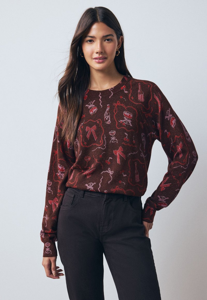 Pull marron à manches longues avec des motifs graphiques festifs rouges et roses, incluant des nœuds et des bouteilles de vin. Coupe décontractée, encolure ronde.