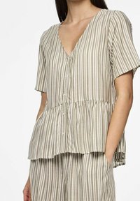 Blusa a maniche corte a righe in beige e bianco sporco con scollatura a V, chiusura con bottoni e orlo peplum. Tessuto morbido con una consistenza leggera.