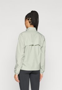 Φωτεινό πράσινο αδιάβροχο μπουφάν με χαλαρή εφαρμογή, ελαστικούς καρπούς και πλάγια πτυχωτή ραφή στο πίσω μέρος. Διαθέτει όρθιο γιακά και λείο, υφασμάτινο υλικό.