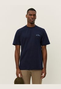 Tricou din bumbac de culoare bleu marin, cu mâneci scurte, guler rotund și un detaliu logo subtil de o nuanță mai deschisă de albastru pe pieptul stâng. Textură netedă.