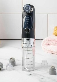 Dispositif de nettoyage StylPro avec un dessus noir, un récipient transparent marqué de mesures et des bouchons gris à proximité. Contient des réglages de contrôle.
