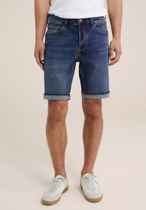 Jeansshorts i mörkblått med en klassisk design och uppvikt kant. Bärs tillsammans med vita sneakers och en ljusfärgad t-shirt.
