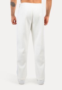 Weiße Sweatpants mit einem elastischen Bund, geraden Beinen und seitlichen Streifen. Weicher Stoff mit glatter Textur. Keine sichtbare Markenkennung oder Muster.