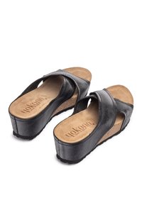 Sandales compensées en cuir noir avec des brides croisées, une semelle intérieure texturée et un intermédiaire en liège. Dotées d'une semelle extérieure en caoutchouc pour l'adhérence.