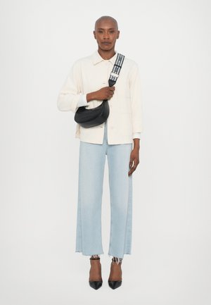 Camicia giacca oversized bianca, jeans a gamba larga azzurri chiari con orli sfrangiati, borsa nera con logo e tacchi a punta neri.
