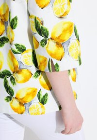 Blusa a maniche corte con stampa di limoni gialli vivaci e foglie verdi su tessuto bianco. Presenta maniche corte con spacchi laterali.