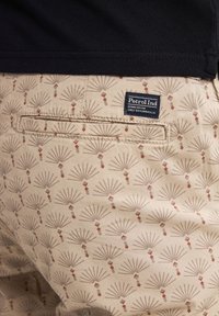 Pantaloni corti in tessuto beige con un motivo a ventaglio in colori tenui, con un piccolo tag di marca sulla tasca posteriore e un design delle tasche piatto e elegante.