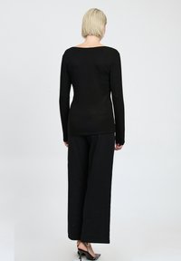 Top lungo nero a maniche lunghe con scollo ampio abbinato a pantaloni neri larghi e sandali con tacco caratterizzati da dettagli borchati.