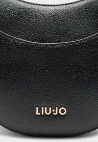 Borsa a tracolla nera in pelle con una superficie liscia, forma arrotondata e logo embossato in oro rosa sul fondo. Dettaglio di cucitura sottile lungo la parte superiore.