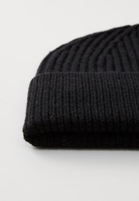 Berretto nero lavorato a maglia con una texture a coste, caratterizzato da un risvolto. Il materiale sembra morbido e caldo, adatto per il freddo.