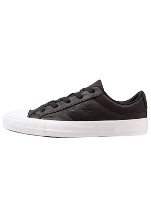 Sneaker en cuir noir avec un embout et une semelle en caoutchouc blanc, doté de lacets noirs et d'un logo étoile subtil sur le côté extérieur. Forme ronde.