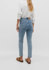 High-rise blue denim jeans with a slim fit, featuring two back pockets and a leather label at the waistband. Paired with a white shirt.