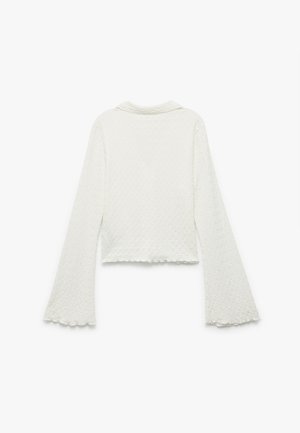 Weißes, kurzes Oberteil aus strukturiertem Stoff mit Glockenärmeln und einem wellenförmigen Saum. Besitzt einen schlichten Kragen mit einem geflochtenen Muster.