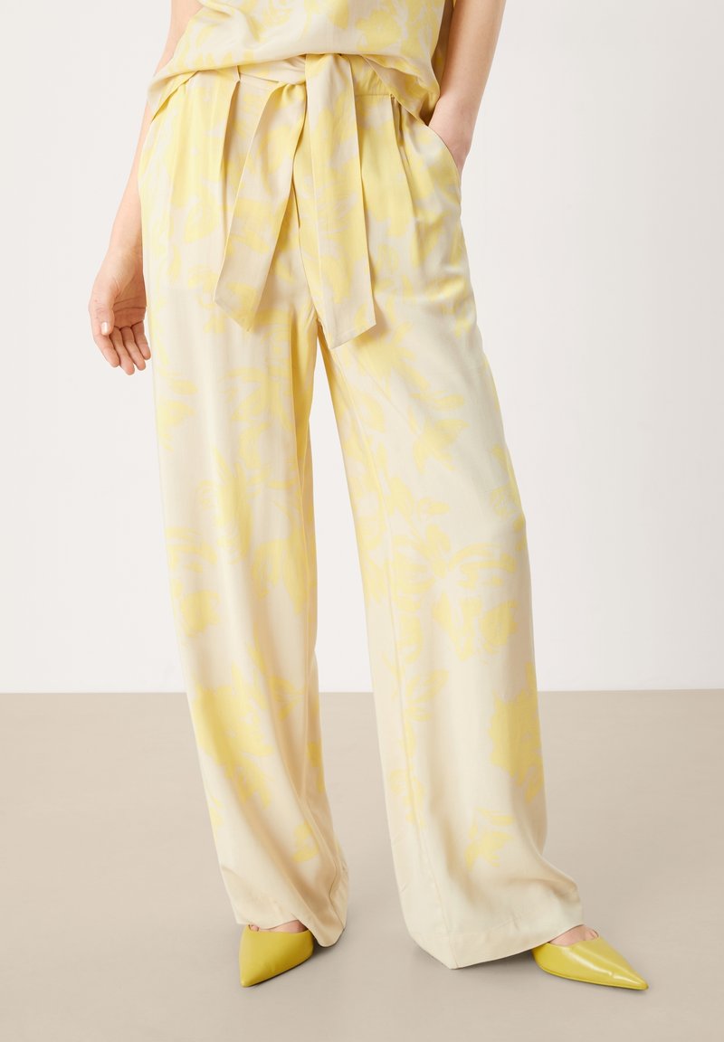 Light yellow trousers with a floral pattern, featuring a tied waistband and side pockets. Paired with pointed yellow shoes.
