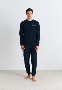 Námornícky dlouhý rukáv košile a odpovídající kalhoty vyrobené z bavlny, s malým bílým logem "Tommy Hilfiger" na hrudi a žebrovanými manžetami.