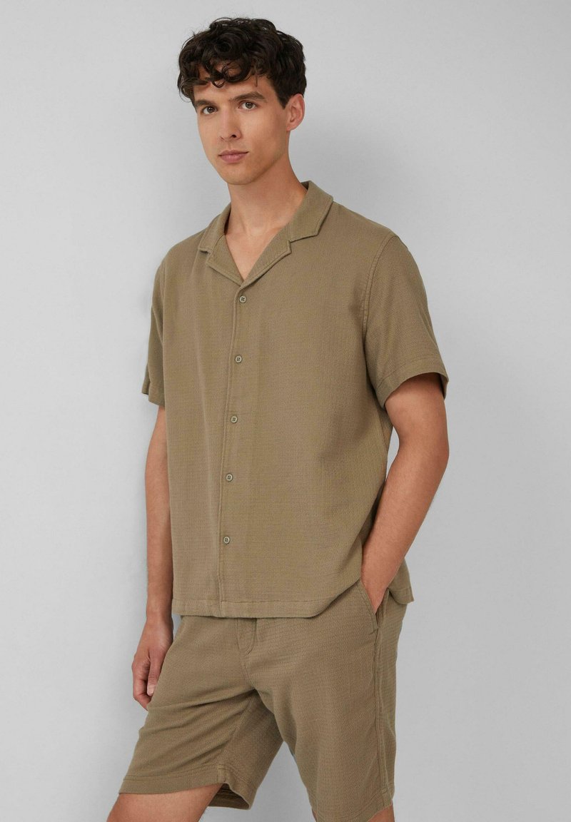 Khaki, kortemouw knoopshirt gemaakt van textuurstof, gecombineerd met bijpassende shorts. Beide kledingstukken hebben een relaxte pasvorm en zakdetails.