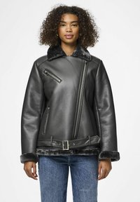 Giacca di pelle nera con zip frontale, hardware in argento, colletto e polsini in finta pelliccia, e design con cintura in vita. Jeansi di denim sotto.
