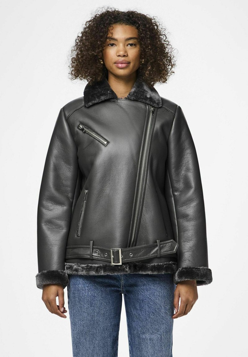 Giacca di pelle nera con zip frontale, hardware in argento, colletto e polsini in finta pelliccia, e design con cintura in vita. Jeansi di denim sotto.