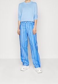 Maglietta a maniche lunghe di colore azzurro chiaro abbinata a pantaloni larghi a righe blu e zoccoli bianchi, caratterizzati da una silhouette rilassata e una texture morbida.