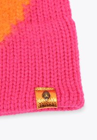 Tessuto lavorato a maglia rosa con un dettaglio arancione e un accento a forma di conchiglia dorata. La texture è morbida e pelosa, con cuciture visibili.