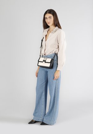 Borsa a tracolla; pelle bianca e nera; forma rettangolare; accessori in argento; modello indossa una camicia marrone chiaro con colletto arricchito e jeans larghi blu.