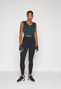Crop top fără mâneci, de culoare verde închis, cu un logo alb; colanți negri cu talie înaltă; pantofi sport alb-negru; mănuși de antrenament fără degete.