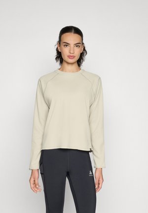 Lys beige langermet topp med en teksturert vaffelmønsterdesign og raglanermer, kombinert med svarte tettsittende leggings.