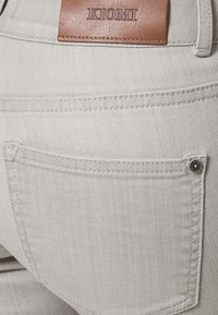 Ljust grå jeans med en bakficka, synlig sömnad längs sömmarna och en brun läderetikett präglad med "KIOMI."