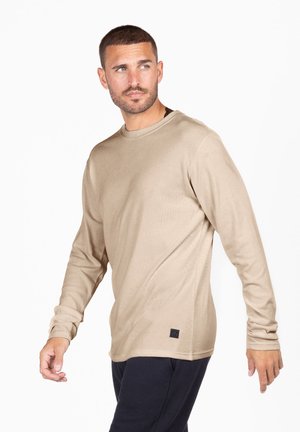 Beige Langarmhemd aus weichem Material mit Rundhalsausschnitt und kleinem schwarzen Logo-Detail am Saum.
