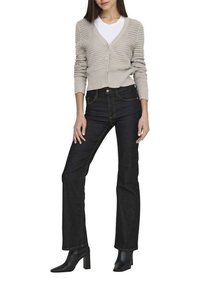 Cardigan en tricot beige clair avec un col en V et une fermeture à boutons sur un t-shirt blanc, associé à un jean en denim foncé taille haute et des bottines noires.